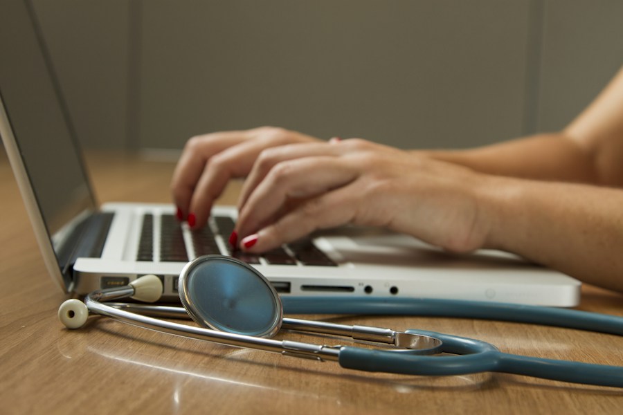 A healthcare professional working on a laptop beside a stethoscope